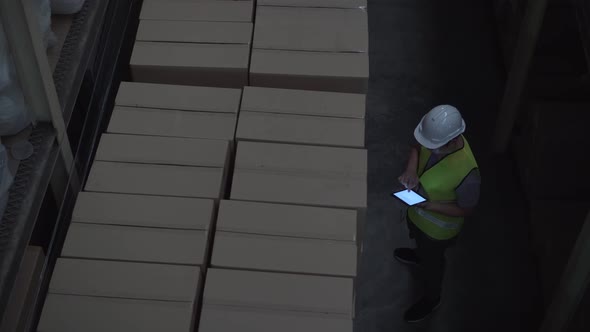 Warehouse Worker Man with Safety Hard Hat is Checking Order Details with Tablet at Inventory Room alt