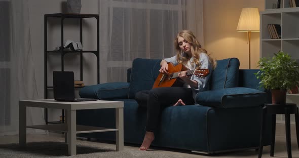 Young Woman Is Playing Sad Love Song on Guitar Sitting in Living Room at Evening Romantic Mood Music alt
