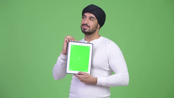 Young Happy Bearded Indian Man Thinking While Showing Digital Tablet