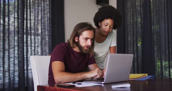 Mixed race couple using laptop and high fiving each other at home alt