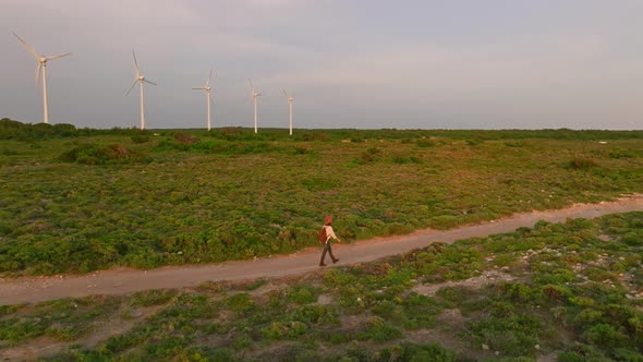 Young traveler woman with a backpack walking along the windmill farm on the shore alt