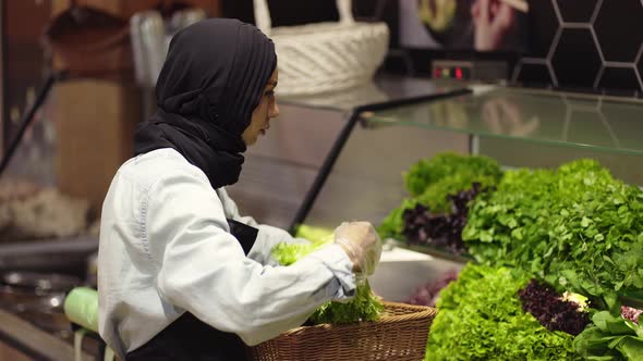 Lady in Hijab Refill the Fresh Greens on the Shelf at the Supermarket alt