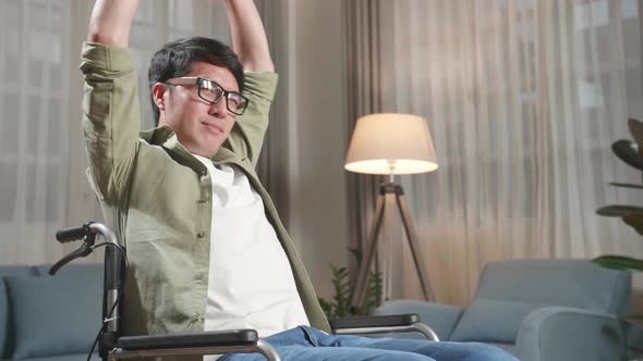 Asian Man Sitting In A Wheelchair And Stretching At Home alt