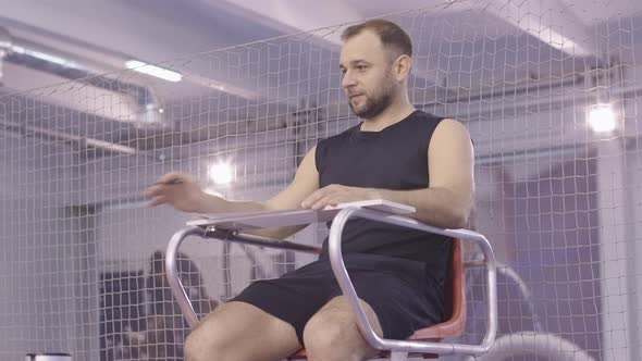 Portrait of Confident Caucasian Judge Sitting on Referee Chair in Gym and Talking. Positive alt