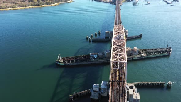 An aerial shot over elevated train tracks crossing a bay in Queens, NY. The camera dolly directly ov alt