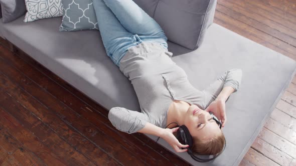 Young beautiful girl lies on a sofa in headphones alt