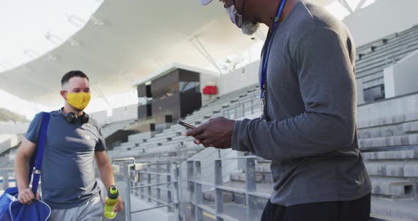Diverse male coach and athlete wearing face mask touching elbows before training session alt
