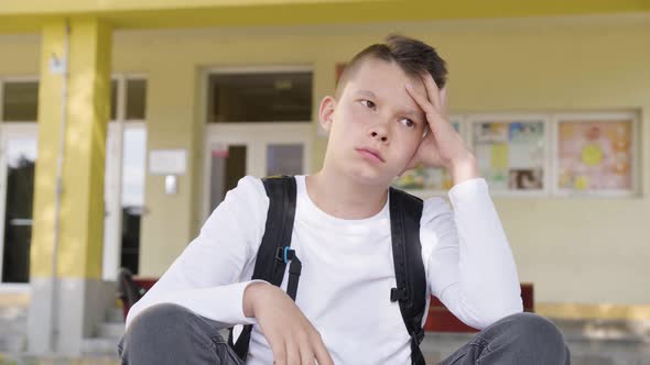 A Caucasian Teenage Boy Thinks About Something As He Sits in Front of School  Closeup