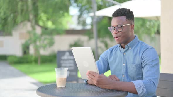 African Man Making Video Call on Tablet in Outdoor Cafe alt