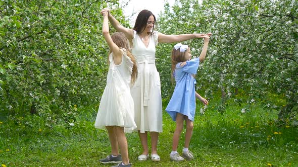 Adorable Little Girls with Young Mother in Blooming Garden on Beautiful Spring Day Having Fun alt