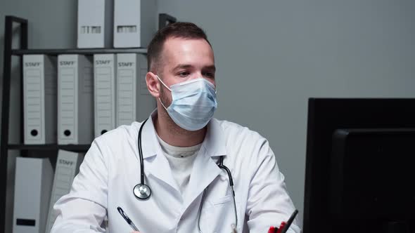 Man Doctor Wearing Protective Face Mask Medical Gown Sitting and Writing Documents Typing on alt