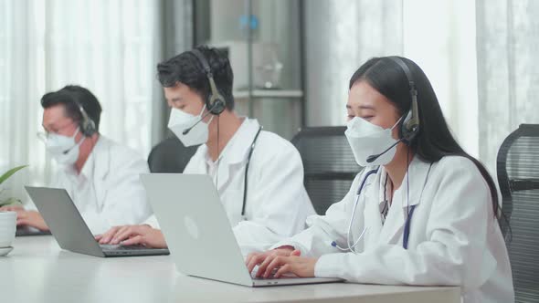 Three Asian Doctors With Stethoscopes In Headsets And Masks Working As Call Centre Agent alt