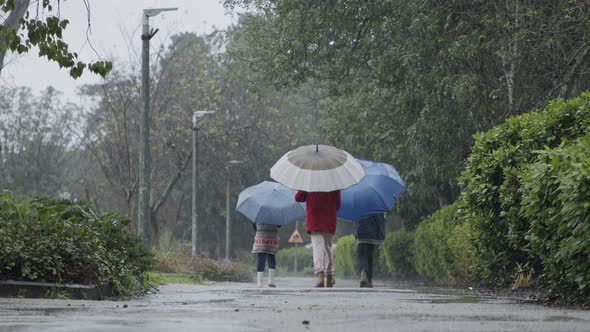Three kids running happy in the rain and puddles with umbrellas alt