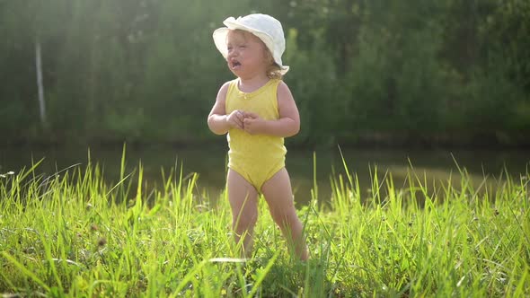 Little Funny Cute Blonde Girl Child Toddler in Yellow Bodysuit and White Hat Crying Walking in Field