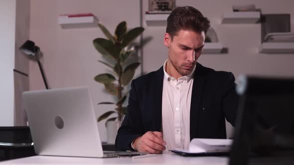 Man Employer Looking at Resume and Working with Laptop Sitting at Table in Office Spbi alt