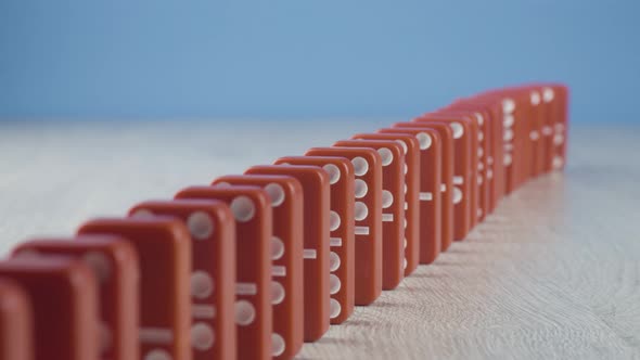 Domino Effect - a Series of Red Dominoes Falling Down the Chain on Blue Background alt