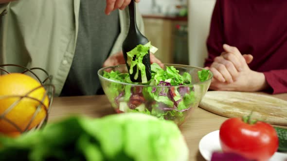 An Attractive Man is Mixing the Salad and Talking with His Friend