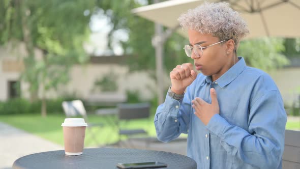 Young African Woman with Coffee Coughing in Outdoor Cafe alt