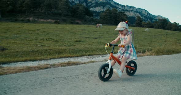 Preschool Girl Ride on Balance Bike on Summer Vacation Along Mountain Meadow alt