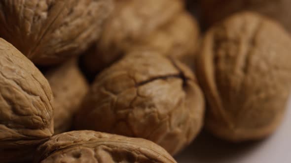 Cinematic, rotating shot of walnuts in their shells on a white surface - WALNUTS  alt