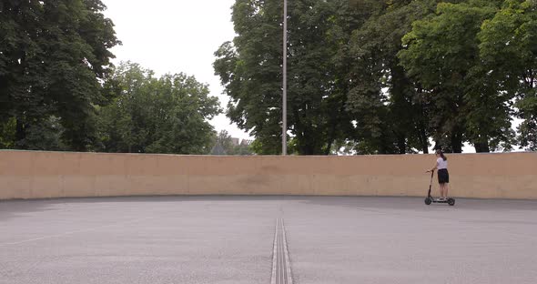 Side view. Attractive girl riding an electric city shared scooter in the street. alt