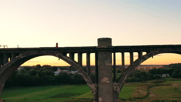 Female Runner Crossing an Old Bridge Is Being Filmed From Afar alt