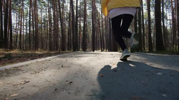 Rear view of an active sportswoman running in a city park, fashionable sports leggings, sneakers. alt