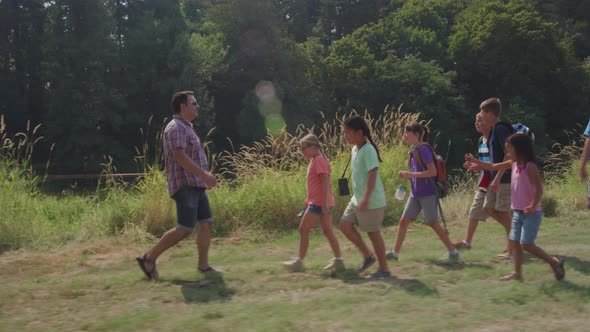 Kids at summer camp hiking by pond with leader