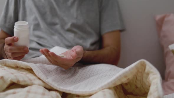 Asian man taking pills into the palm of his hand while in the bedroom at home.