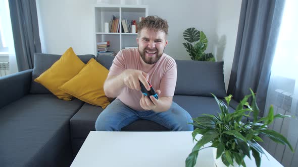 Attractive Man with Bristle and Toothy Grin Holding Joystick and Playing Videogames on Tv Sits at alt