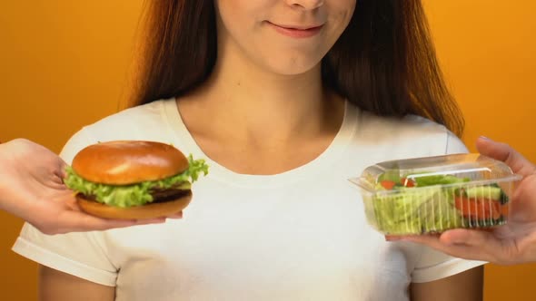 Hungry Woman Choosing Fatty Hamburger Instead of Green Salad, Risk of Overweight alt