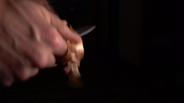 Man Peels An Onion With A Knife On A Black Background