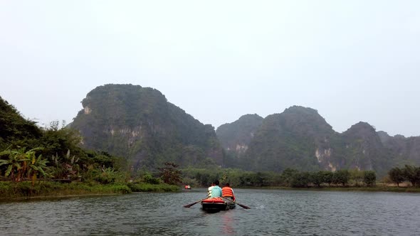 Tour boat with tourists and guide paddling on Day River overlooking limestone Kerst mountain landsca alt