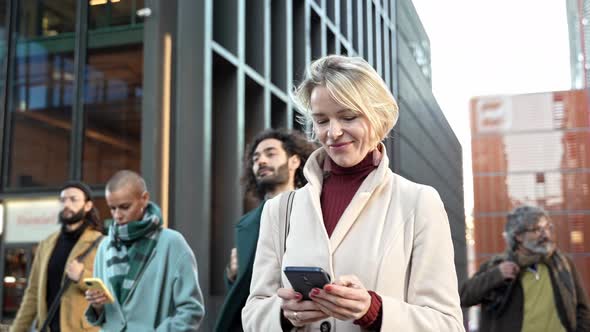 Young Professional Business Woman Walking While Using Phone Messaging Writing Texts After Work in a alt