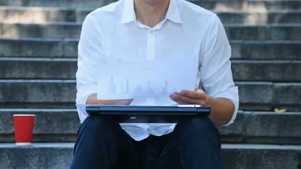 Broker Sitting On Stairs And Examines Financial Statements.
