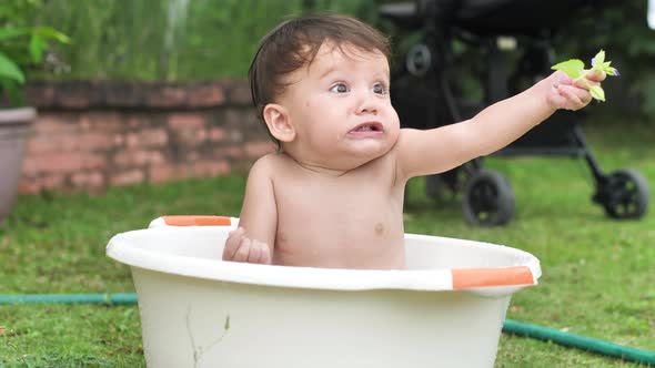 A Small Beautiful Child Sits in a Round Light Basin Holds a Flower at Arm's Length and Looks Around alt
