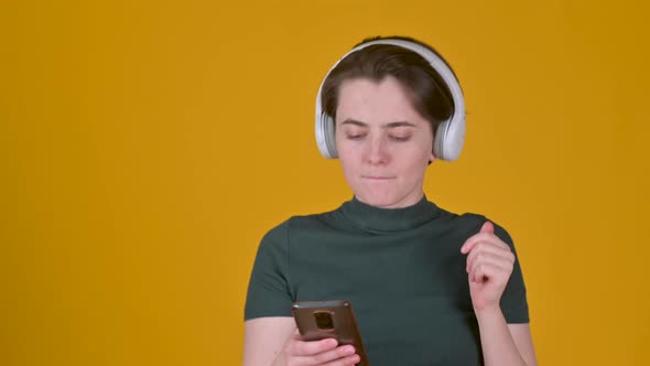 Young girl with headphones listens to music and dances isolated on yellow background
