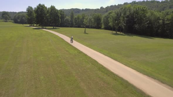 Man Mountain Bike Ride Outdoor in Nature Down a Side Walk in Sunny Day Aerial Drone Follow Wide Shot