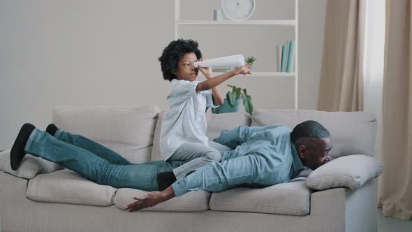 Cheerful African American Family Mature Father Lies on Couch in Room Plays with Little Daughter Cute alt