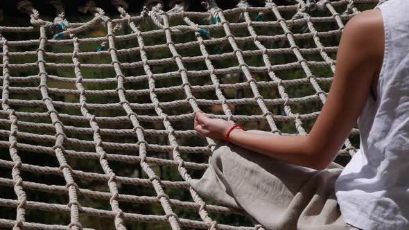 A Young Woman Meditates in the Lotus Position Sitting on a Rope Net on a Sunny Summer Day