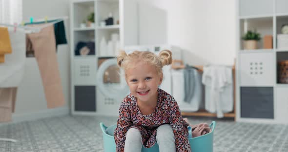 A Beautiful Little Girl with Blonde Hair and Blue Eyes in a Colorful Dress Sits in a Bowl with alt