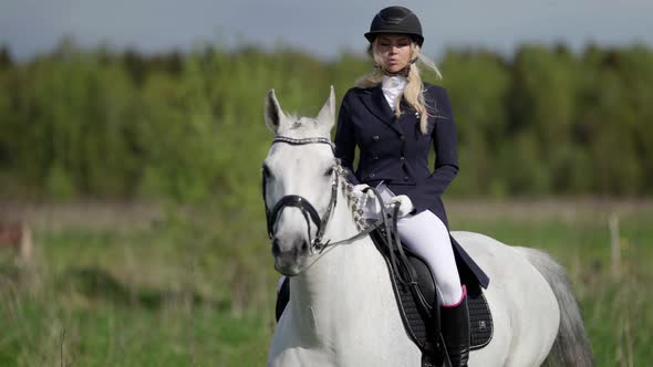 a Blonde in a Jockey Uniform Rides in the Saddle on a White Horse alt