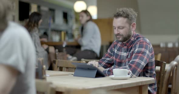 Man using digital tablet and drinking coffee while sitting in pub