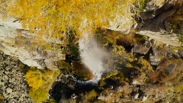 Top Down View Over the Waterfall Running Down the Rocky Cliff Covered with Autumn Foliage. alt