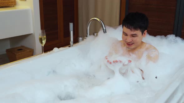 man washing body and playing bubble foam in bathtub
