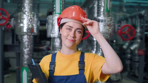 Portrait of a young female engineer standing in a production room and smiling. alt
