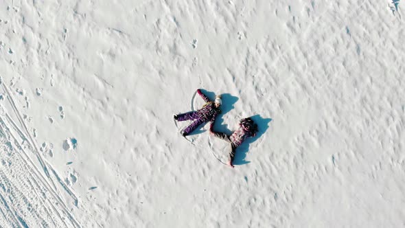 Aerial View From Above of Children Lying on White Snow in Bright Sunshine and Making Snow Angels