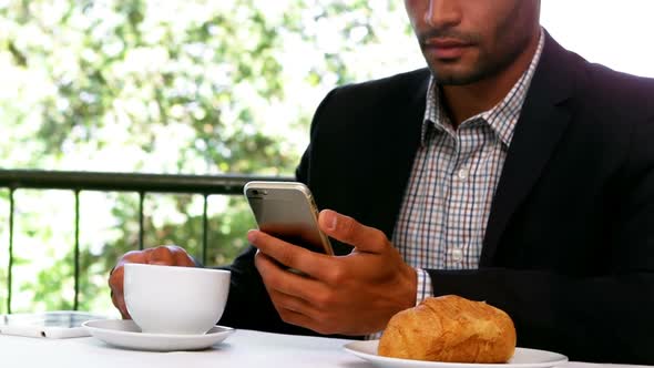 Businessman using mobile phone while having breakfast alt