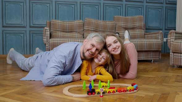 Young Mother and Father Playing with Child Daughter Riding Toy Train on Wooden Railroad Game at Home alt
