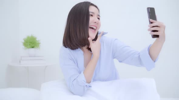 apanese female using smartphone making vlog video to social media on bed in bedroom. alt